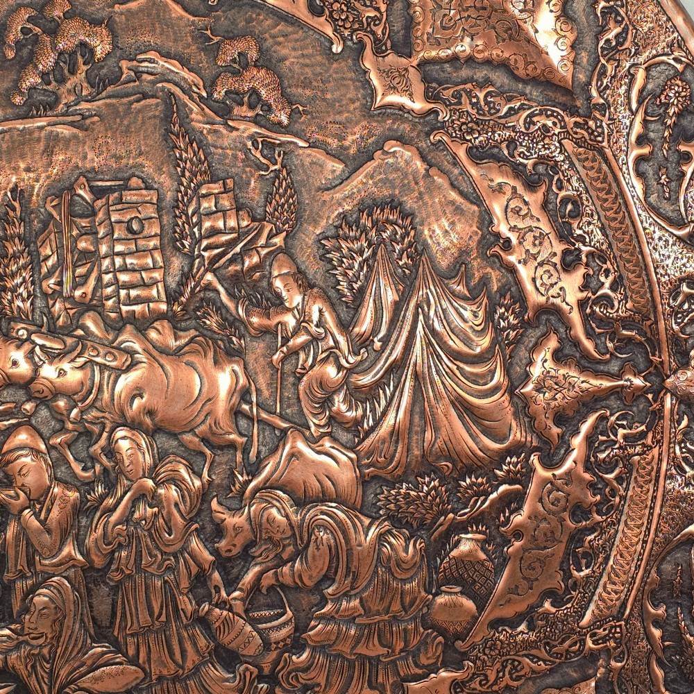 A circular Persian copper charger featuring detailed central repousse relief surrounded by intricate arabesque and paisley borders. View VI