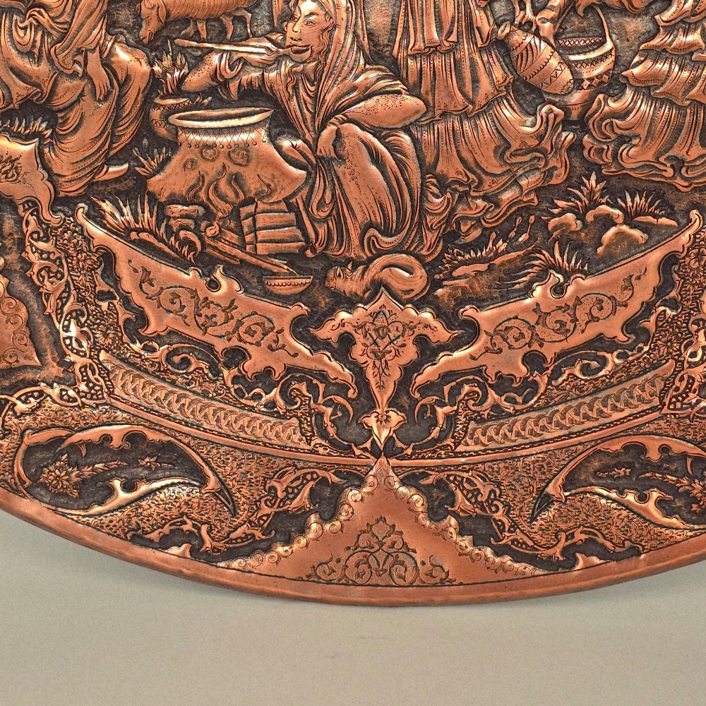 A circular Persian copper charger featuring detailed central repousse relief surrounded by intricate arabesque and paisley borders. View VII