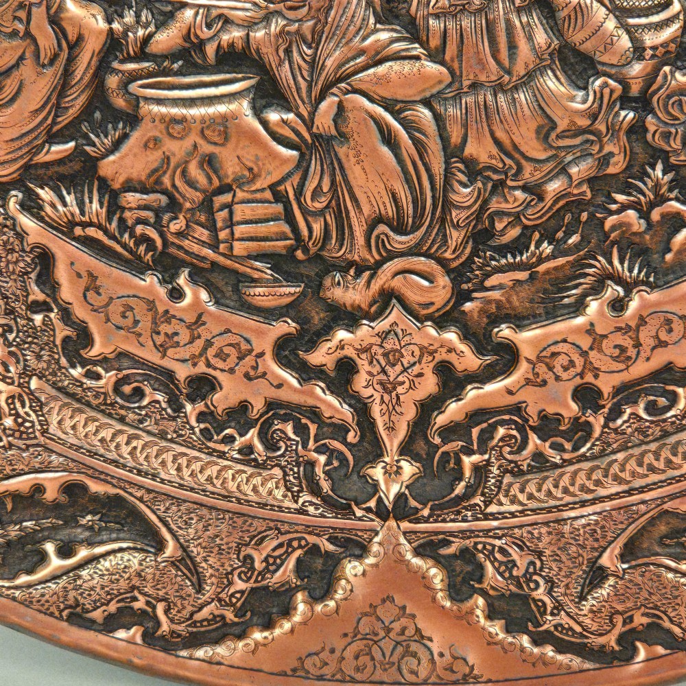 A circular Persian copper charger featuring detailed central repousse relief surrounded by intricate arabesque and paisley borders. View IX