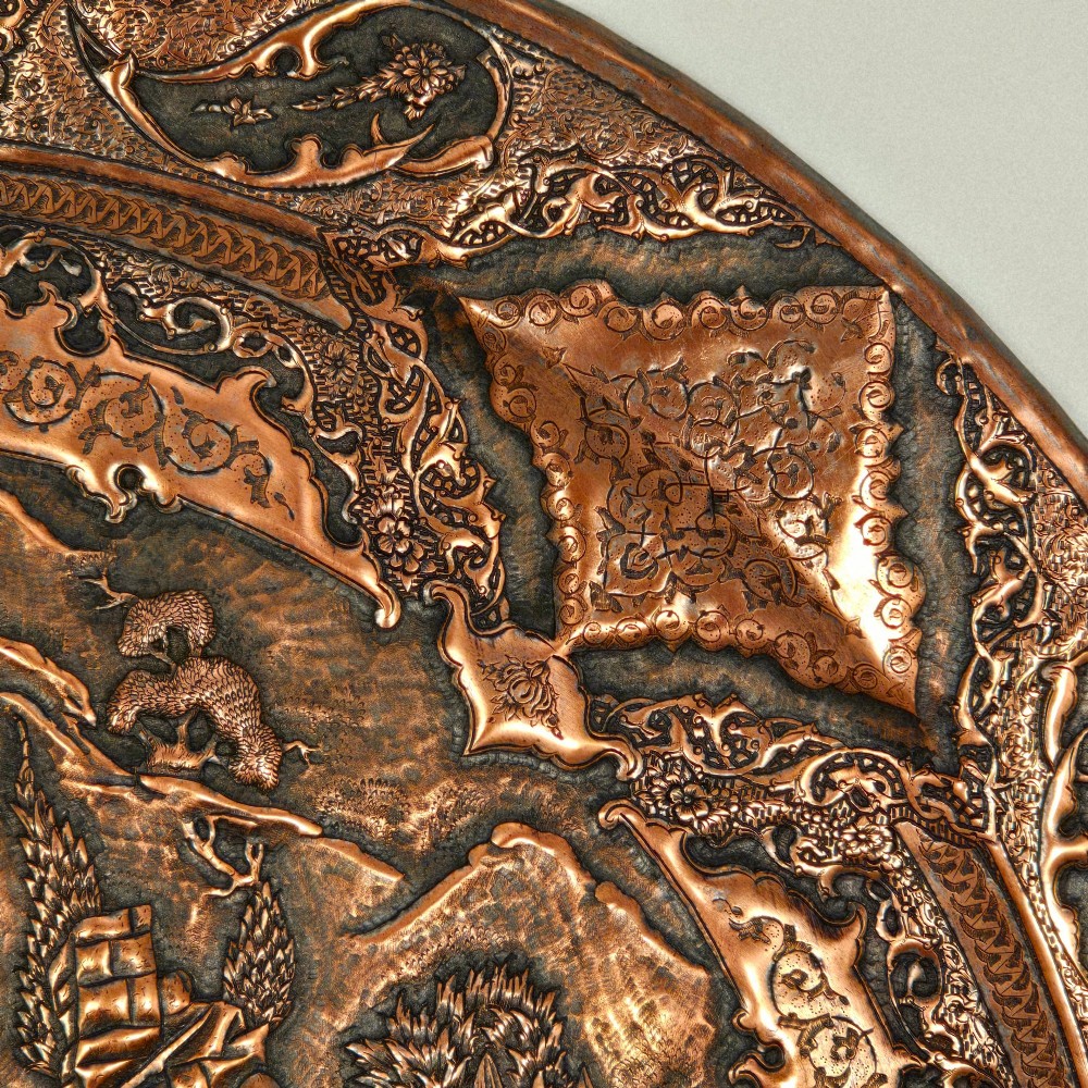 A circular Persian copper charger featuring detailed central repousse relief surrounded by intricate arabesque and paisley borders. View X