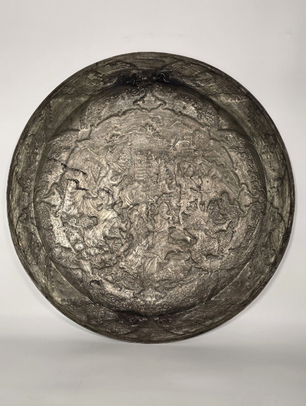 A circular Persian copper charger featuring detailed central repousse relief surrounded by intricate arabesque and paisley borders. View XII