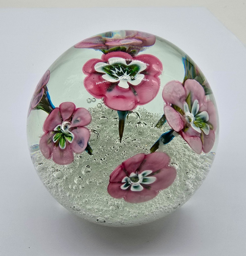 A pair of spherical clear glass paperweights containing pink lampwork flowers above a white bubble base layer. View II