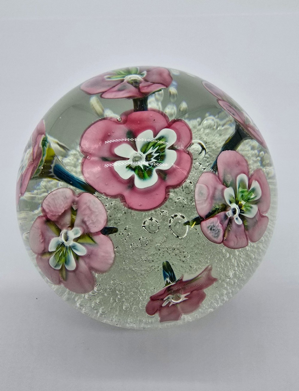 A pair of spherical clear glass paperweights containing pink lampwork flowers above a white bubble base layer. View V