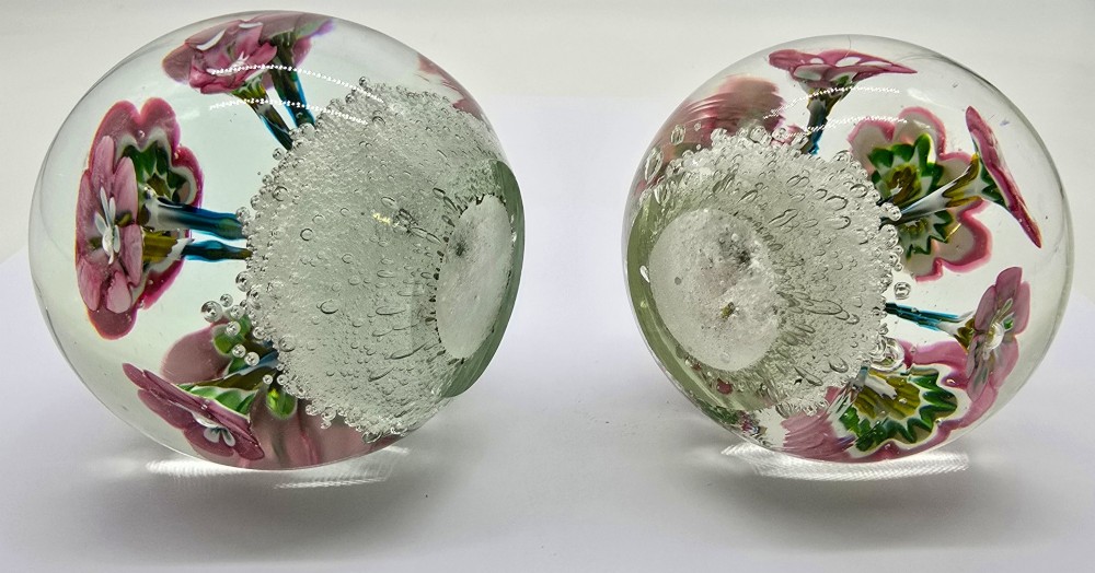 A pair of spherical clear glass paperweights containing pink lampwork flowers above a white bubble base layer. View VII