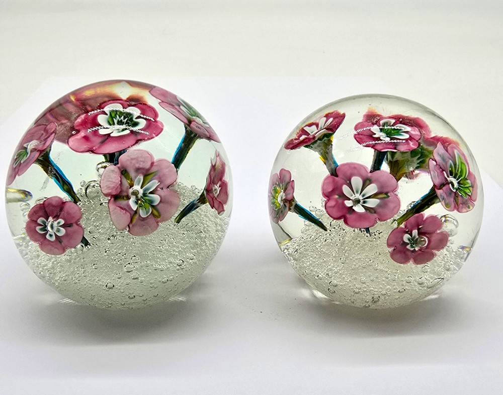 A pair of spherical clear glass paperweights containing pink lampwork flowers above a white bubble base layer. View VIII