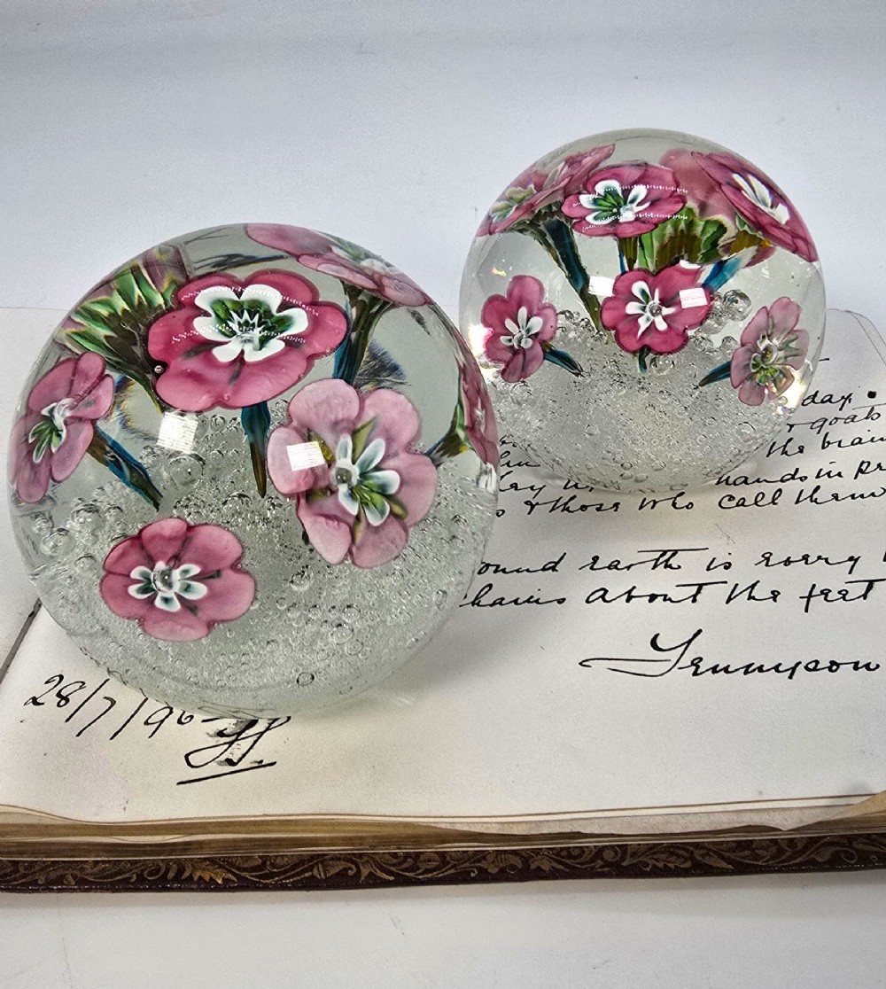 A pair of spherical clear glass paperweights containing pink lampwork flowers above a white bubble base layer. View X