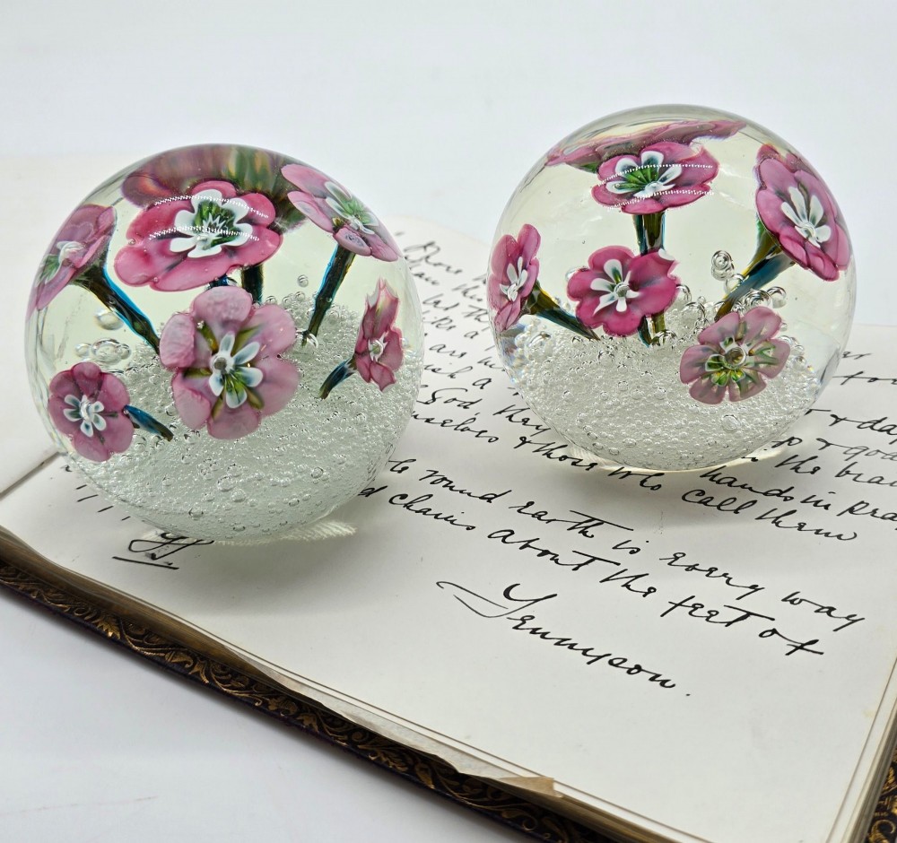 A pair of spherical clear glass paperweights containing pink lampwork flowers above a white bubble base layer. View XI