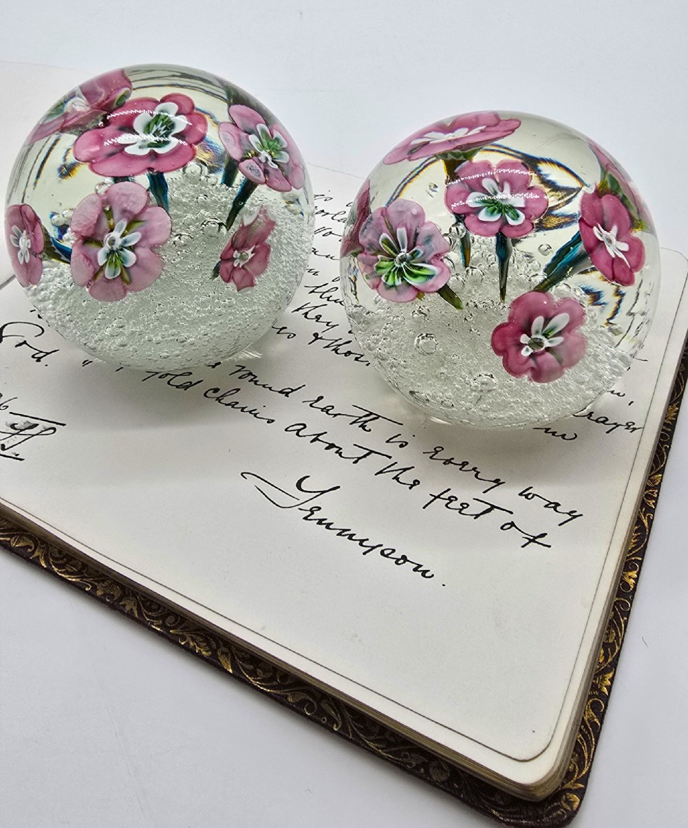A pair of spherical clear glass paperweights containing pink lampwork flowers above a white bubble base layer. View XII
