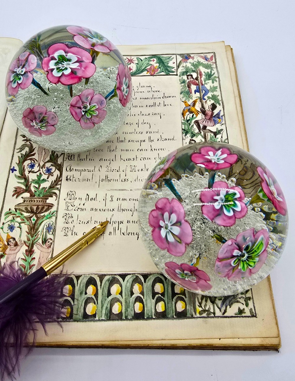 A pair of spherical clear glass paperweights containing pink lampwork flowers above a white bubble base layer. View XV
