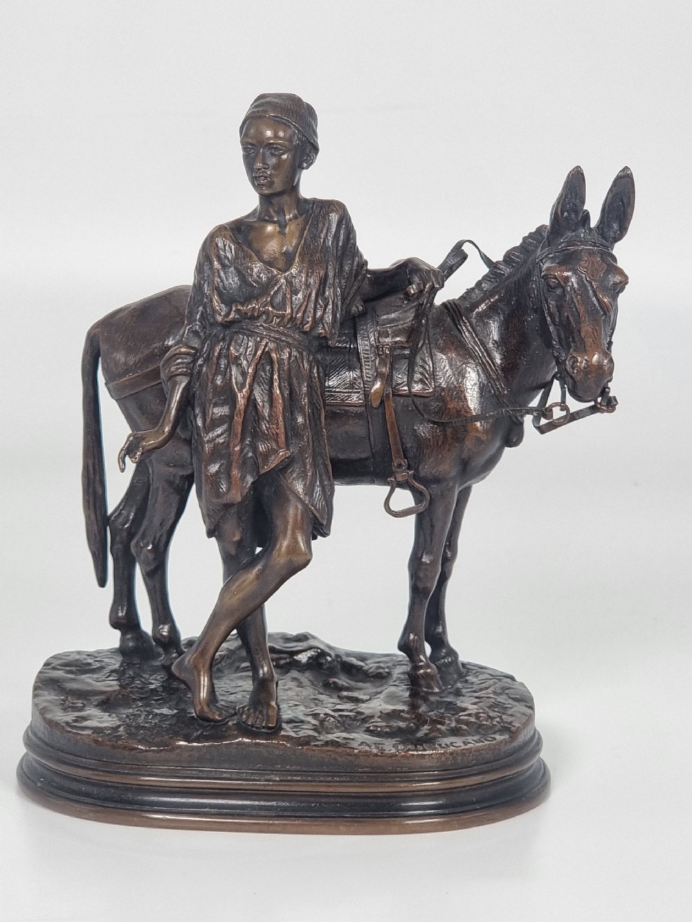A patinated bronze sculpture depicting an Egyptian man leaning against a saddled donkey on an oval base.