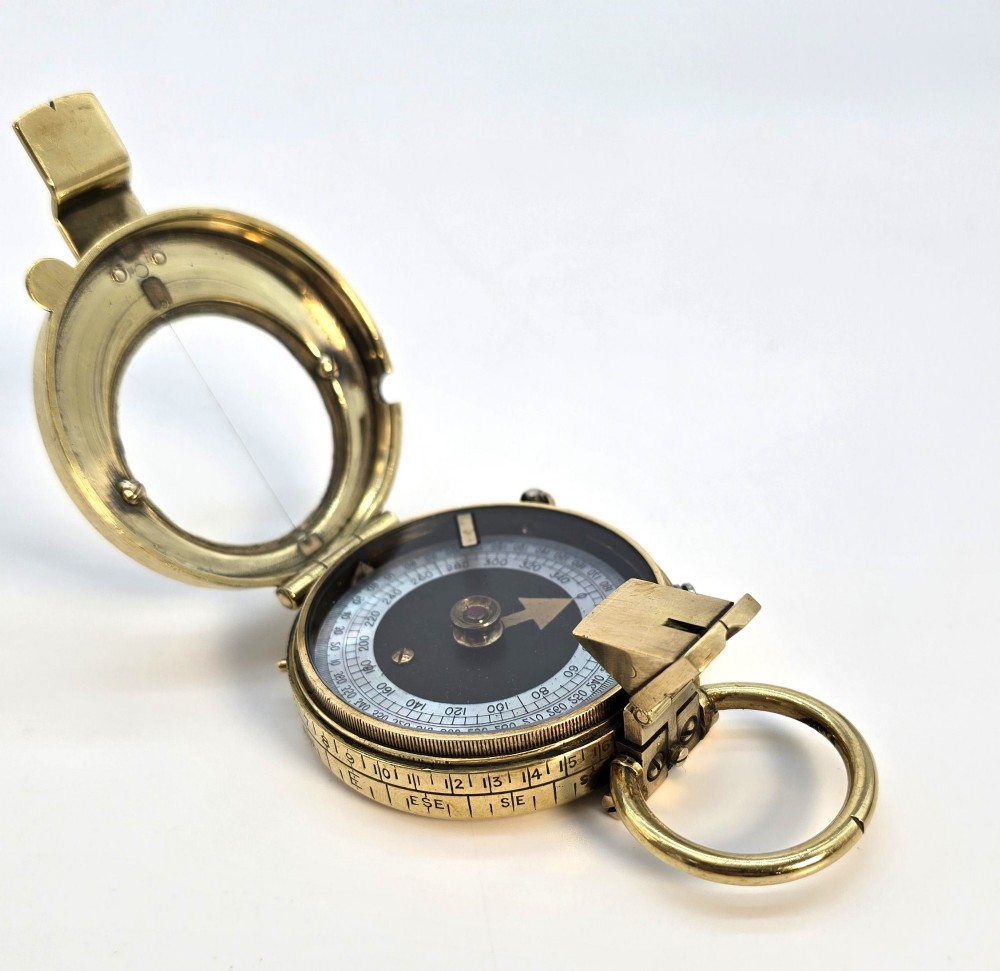An antique Edwardian brass pocket compass with an open hinged lid featuring a glass window, an engraved internal dial, and an attached thumb ring.
