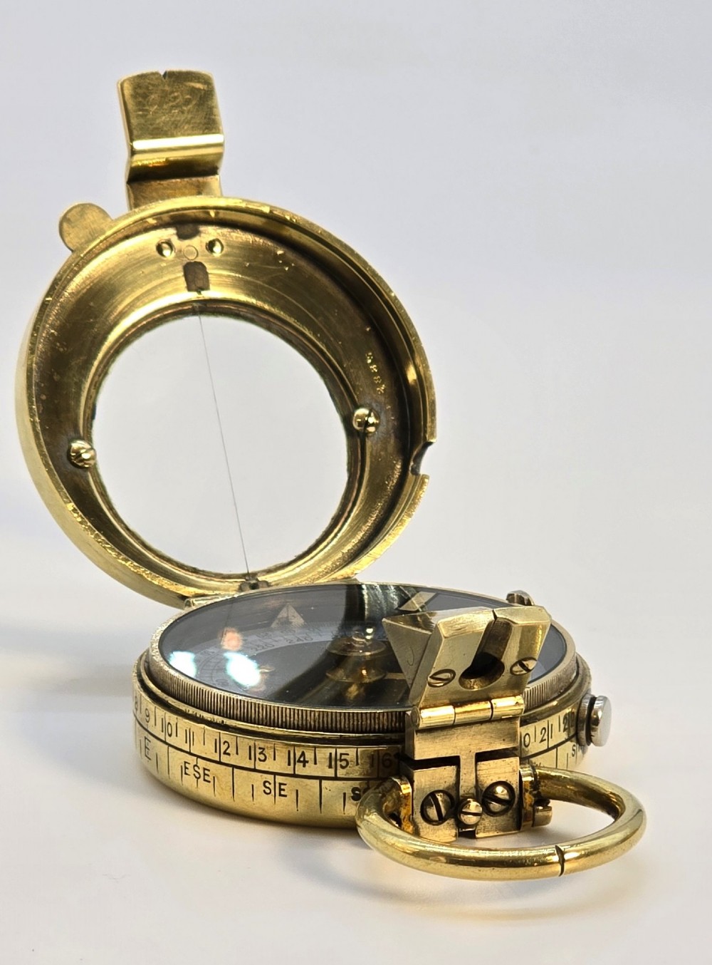 An antique Edwardian brass pocket compass with an open hinged lid featuring a glass window, an engraved internal dial, and an attached thumb ring. View II