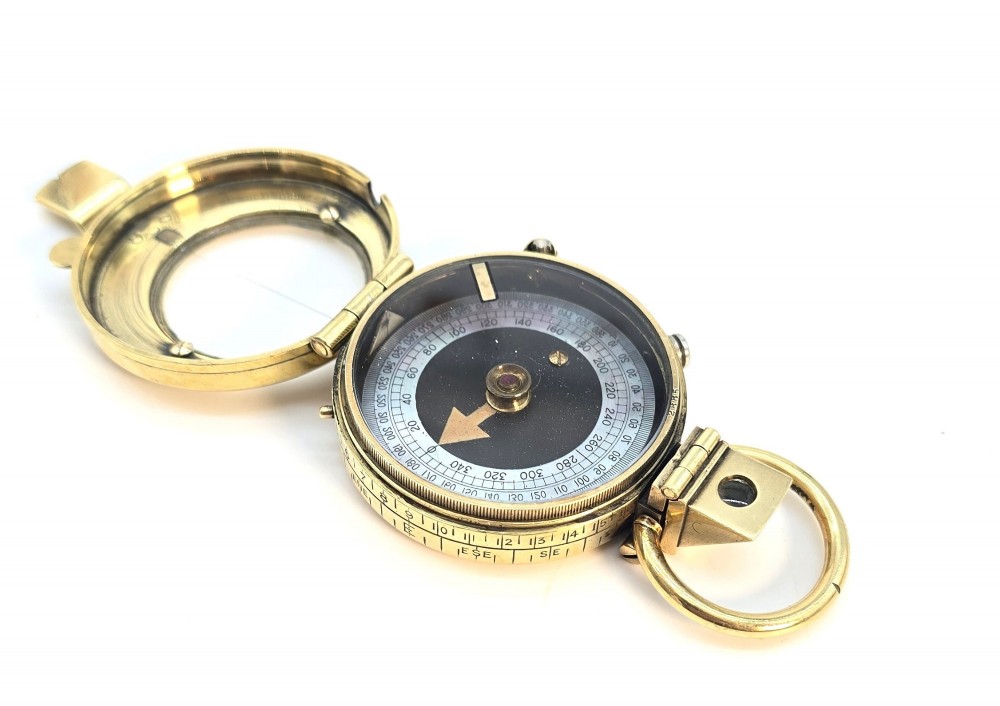 An antique Edwardian brass pocket compass with an open hinged lid featuring a glass window, an engraved internal dial, and an attached thumb ring. View VI