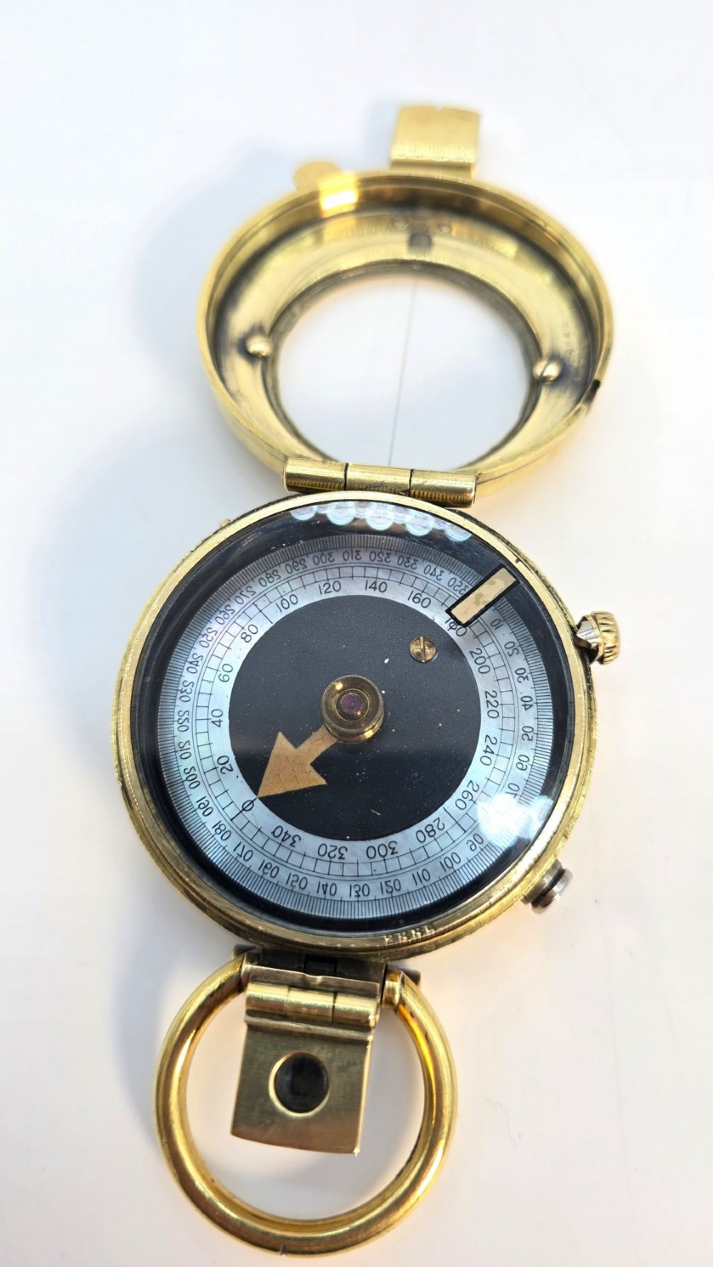 An antique Edwardian brass pocket compass with an open hinged lid featuring a glass window, an engraved internal dial, and an attached thumb ring. View VII