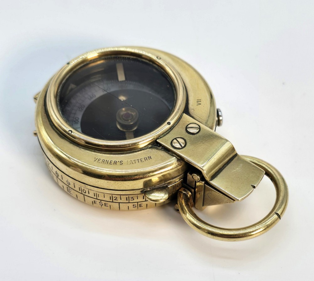 An antique Edwardian brass pocket compass with an open hinged lid featuring a glass window, an engraved internal dial, and an attached thumb ring. View VIII