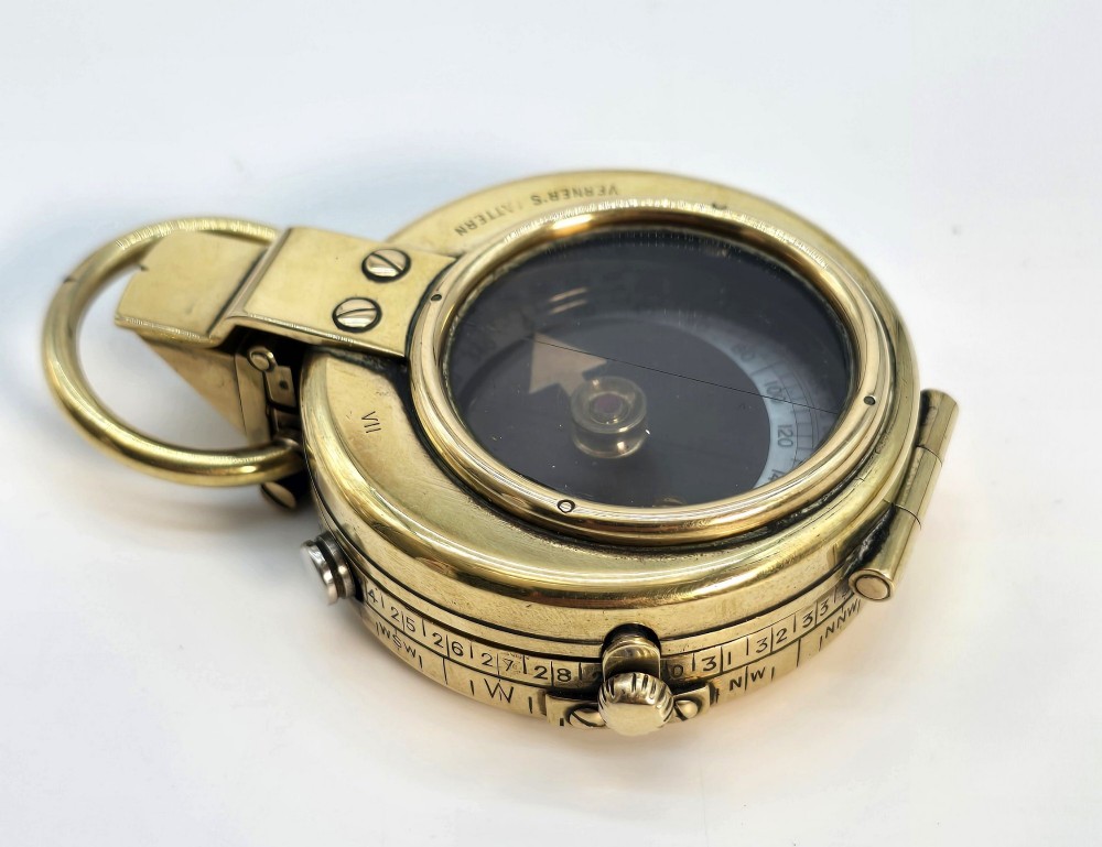 An antique Edwardian brass pocket compass with an open hinged lid featuring a glass window, an engraved internal dial, and an attached thumb ring. View IX