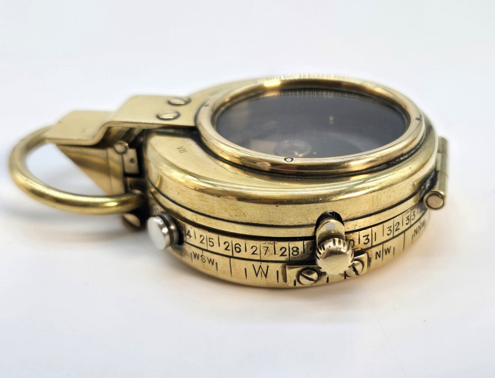 An antique Edwardian brass pocket compass with an open hinged lid featuring a glass window, an engraved internal dial, and an attached thumb ring. View X