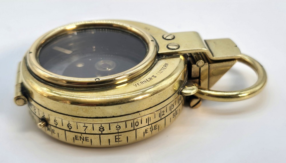 An antique Edwardian brass pocket compass with an open hinged lid featuring a glass window, an engraved internal dial, and an attached thumb ring. View XI