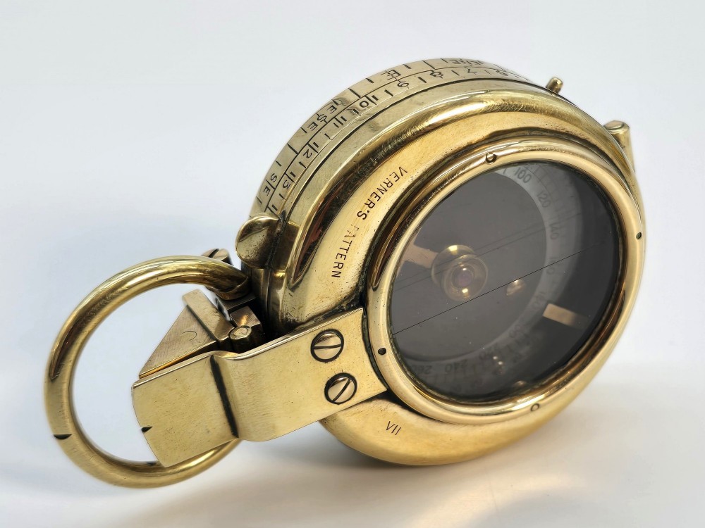 An antique Edwardian brass pocket compass with an open hinged lid featuring a glass window, an engraved internal dial, and an attached thumb ring. View XII