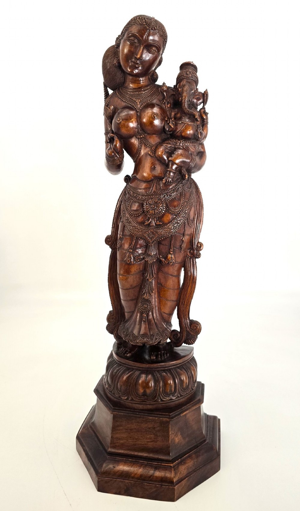 A hand-carved dark wood statue depicting the Goddess Parvati holding infant Ganesha, mounted on an octagonal wooden base. View II