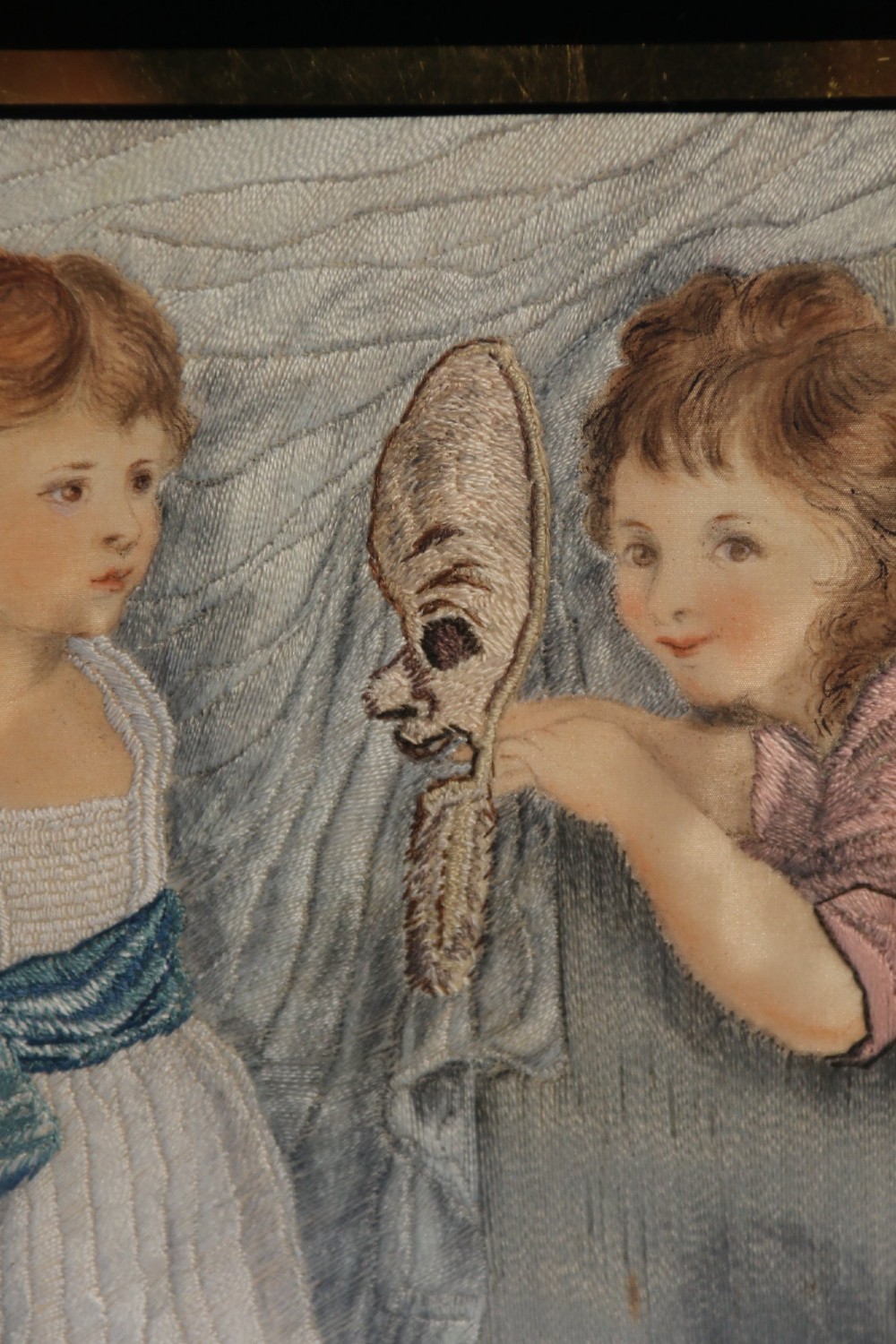 A framed Georgian silk needlework picture depicting two young children with a mask, mounted in a black eglomise frame with gold leaf detailing. View IV