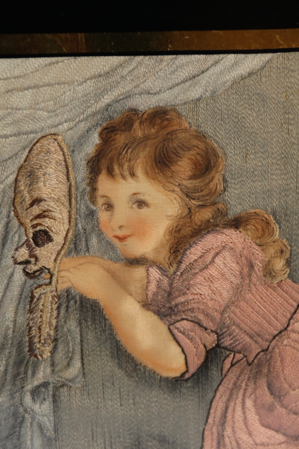A framed Georgian silk needlework picture depicting two young children with a mask, mounted in a black eglomise frame with gold leaf detailing. View IX
