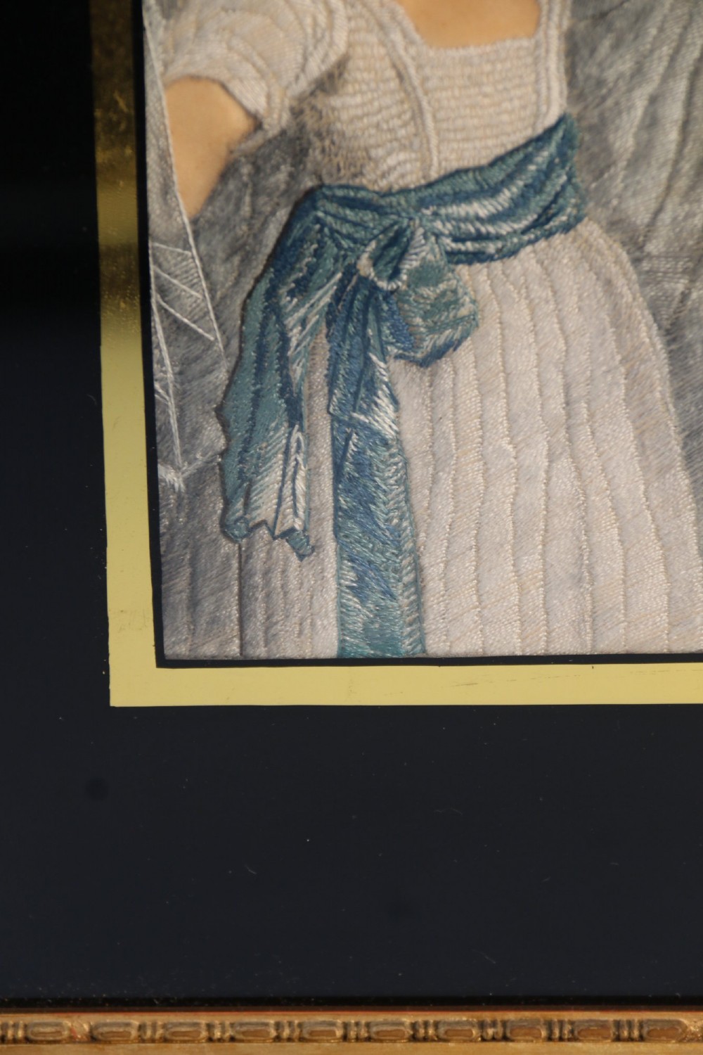 A framed Georgian silk needlework picture depicting two young children with a mask, mounted in a black eglomise frame with gold leaf detailing. View X
