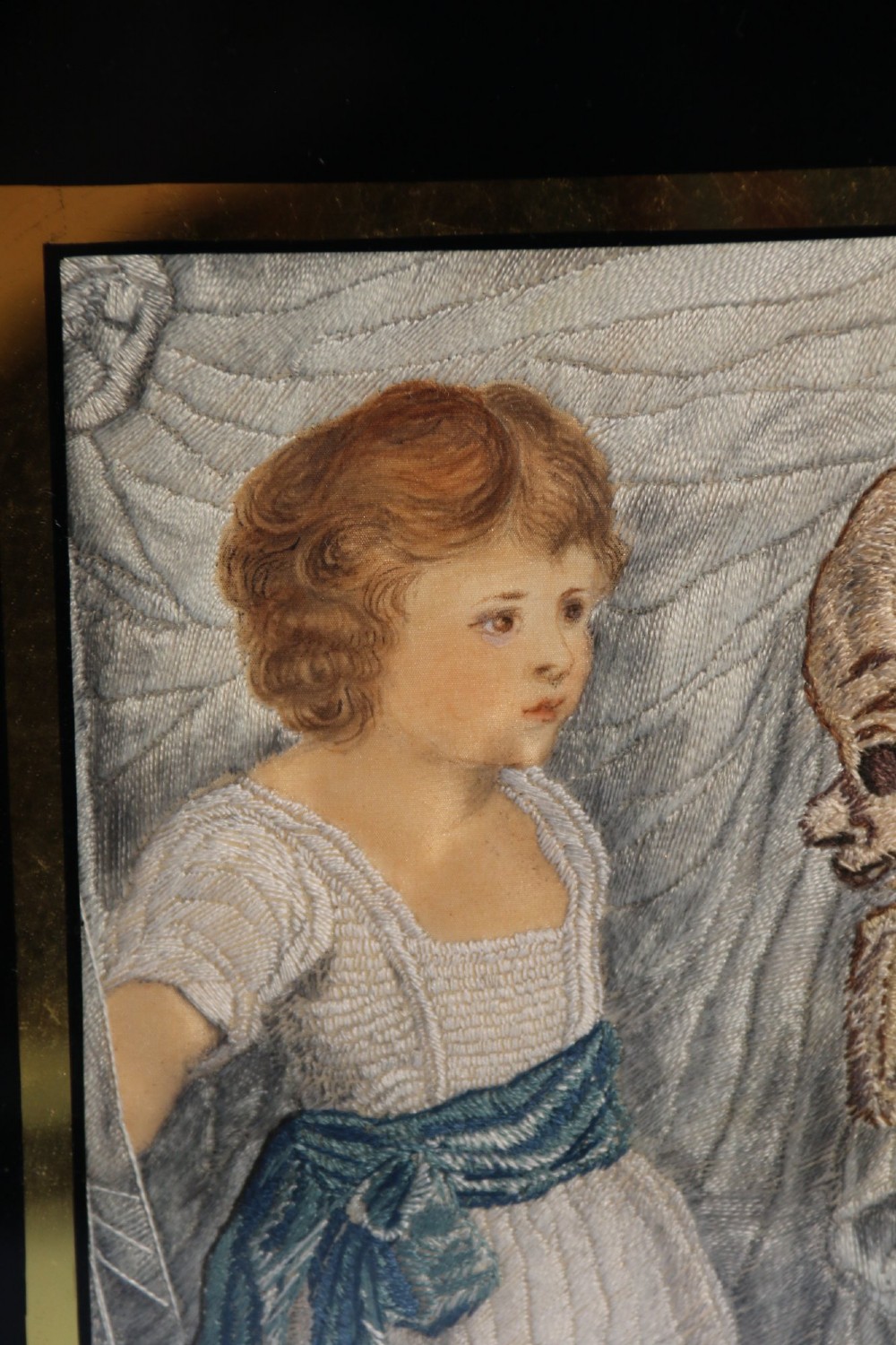 A framed Georgian silk needlework picture depicting two young children with a mask, mounted in a black eglomise frame with gold leaf detailing. View XI