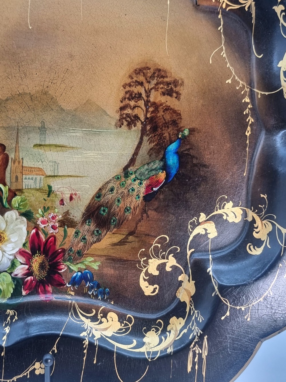 A Victorian shaped papier-mache tray featuring a hand-painted landscape with a castle and peacock surrounded by gold leaf scrollwork on a black background. View IV