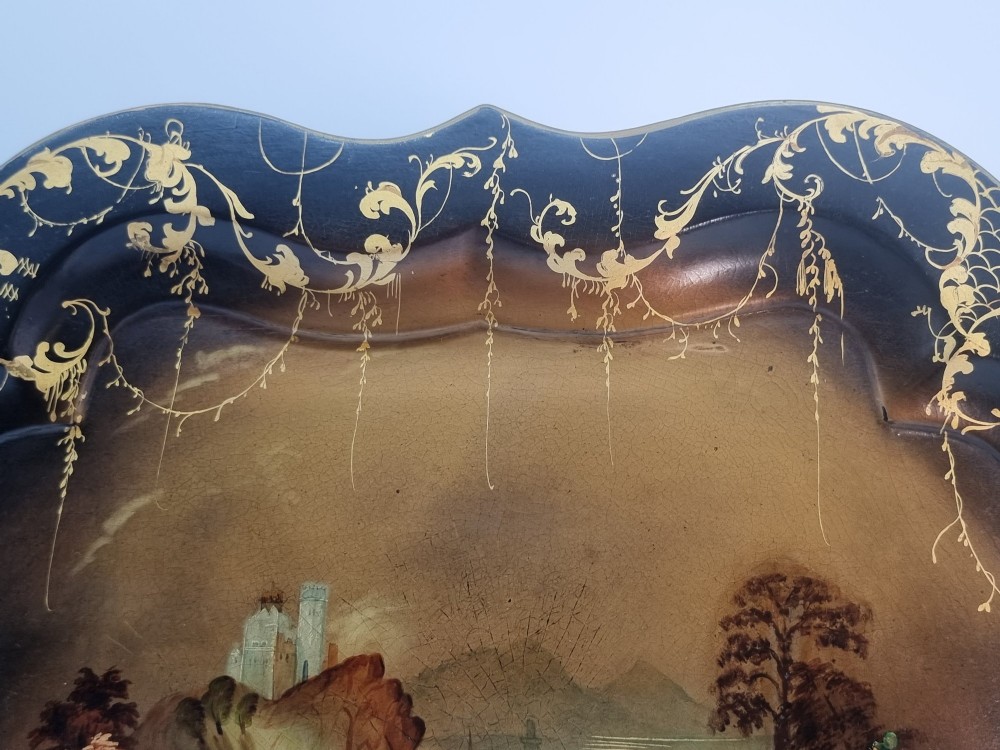A Victorian shaped papier-mache tray featuring a hand-painted landscape with a castle and peacock surrounded by gold leaf scrollwork on a black background. View VII