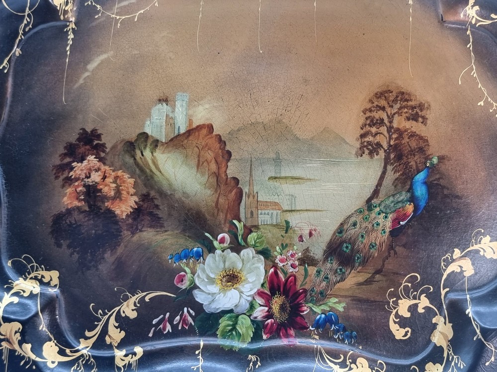 A Victorian shaped papier-mache tray featuring a hand-painted landscape with a castle and peacock surrounded by gold leaf scrollwork on a black background. View VIII