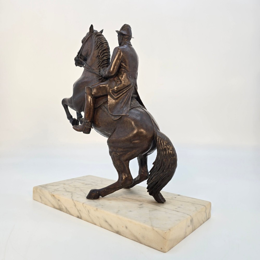A dark bronze equestrian sculpture depicting a uniformed rider atop a rearing horse, mounted on a rectangular cream marble plinth. View II