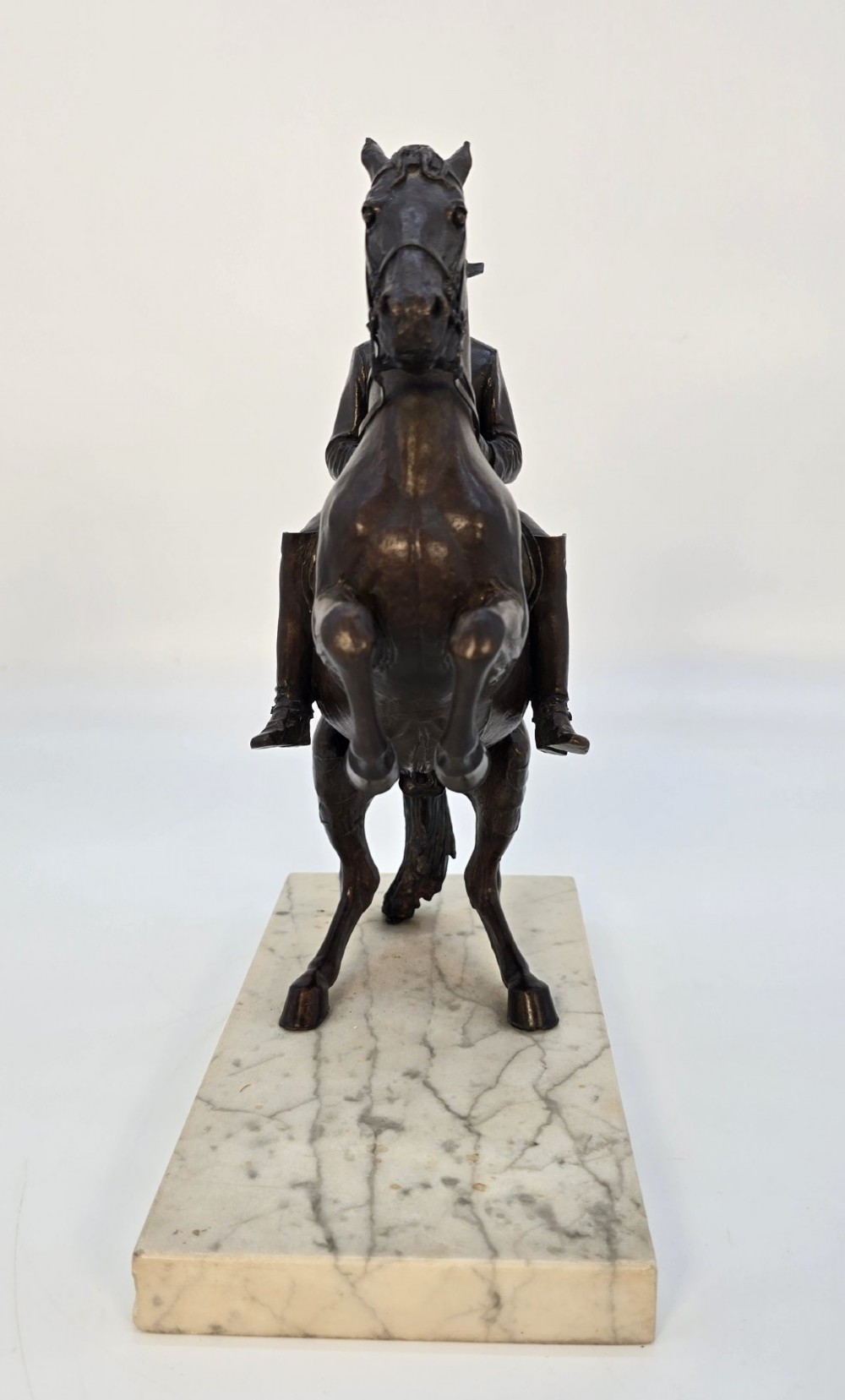 A dark bronze equestrian sculpture depicting a uniformed rider atop a rearing horse, mounted on a rectangular cream marble plinth. View V