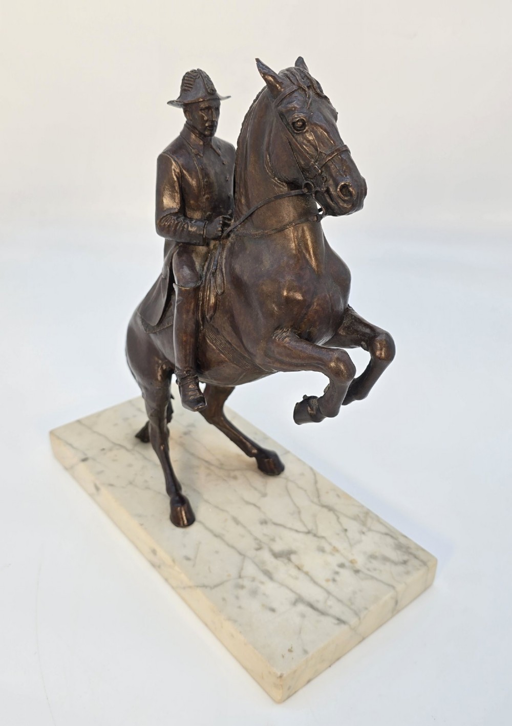 A dark bronze equestrian sculpture depicting a uniformed rider atop a rearing horse, mounted on a rectangular cream marble plinth. View VI