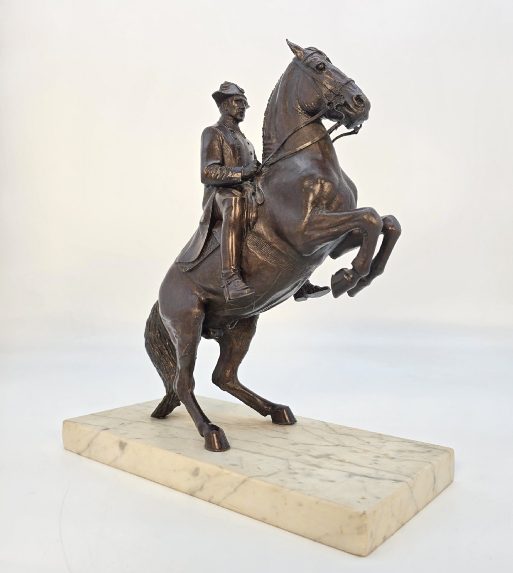 A dark bronze equestrian sculpture depicting a uniformed rider atop a rearing horse, mounted on a rectangular cream marble plinth. View VII