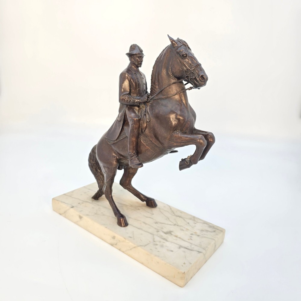 A dark bronze equestrian sculpture depicting a uniformed rider atop a rearing horse, mounted on a rectangular cream marble plinth. View VIII