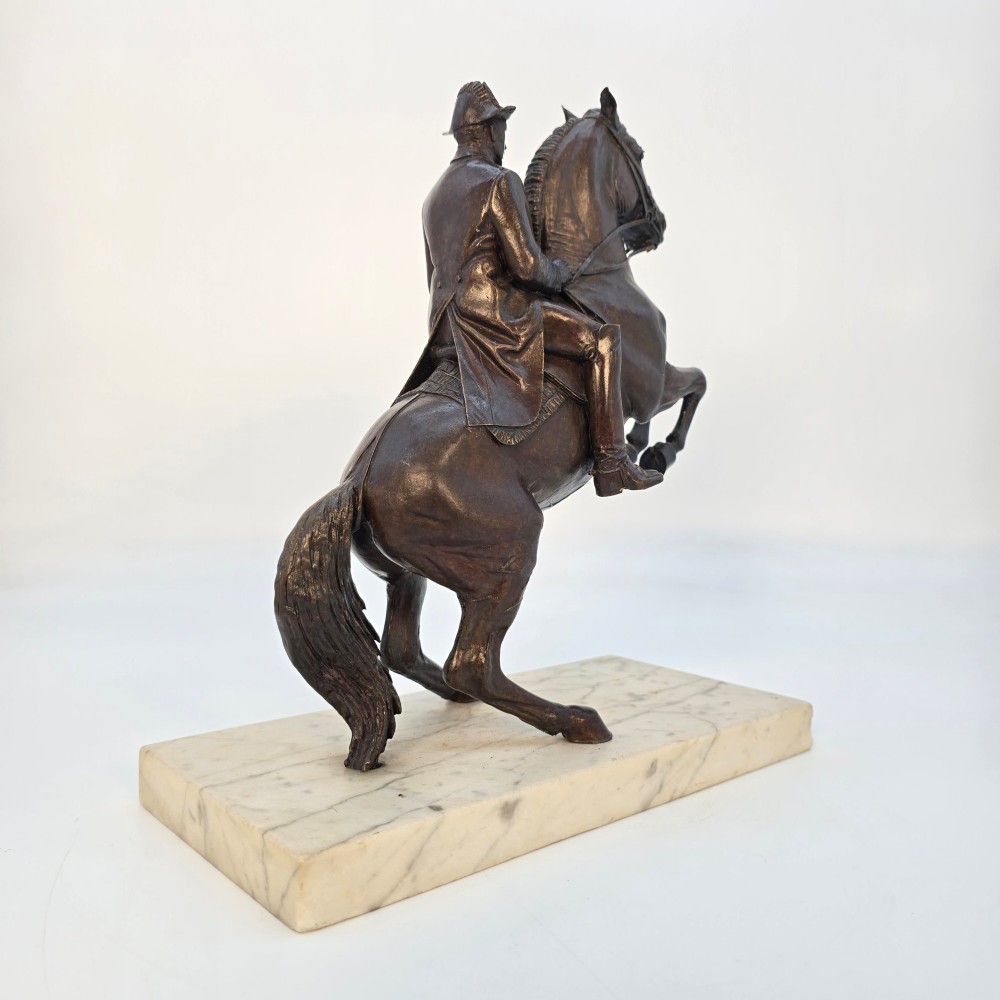 A dark bronze equestrian sculpture depicting a uniformed rider atop a rearing horse, mounted on a rectangular cream marble plinth. View XV