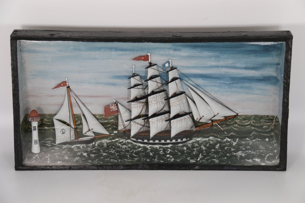 A nineteenth-century glass-fronted black wooden shadow box featuring a carved and painted diorama of two sailing ships and a lighthouse on a textured sea.