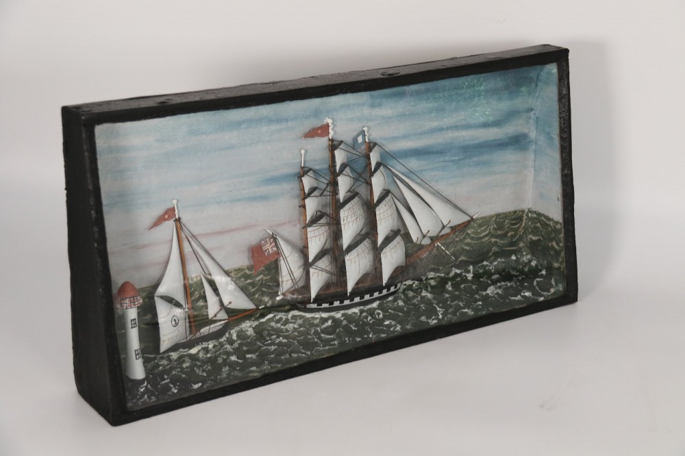 A nineteenth-century glass-fronted black wooden shadow box featuring a carved and painted diorama of two sailing ships and a lighthouse on a textured sea. View III