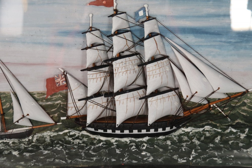 A nineteenth-century glass-fronted black wooden shadow box featuring a carved and painted diorama of two sailing ships and a lighthouse on a textured sea. View VII