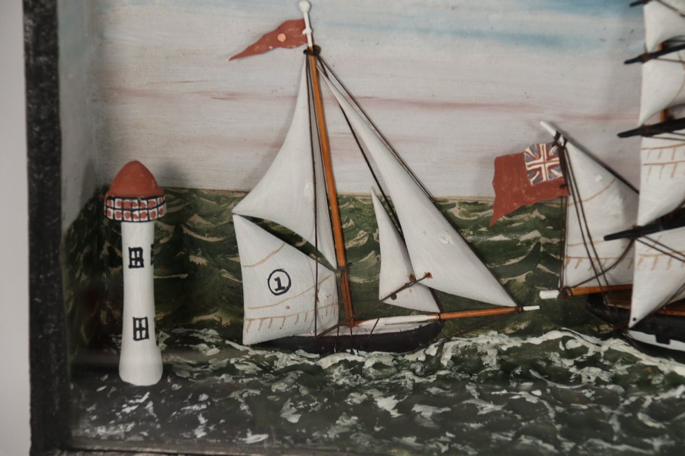 A nineteenth-century glass-fronted black wooden shadow box featuring a carved and painted diorama of two sailing ships and a lighthouse on a textured sea. View VIII