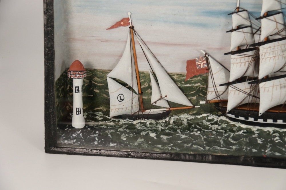 A nineteenth-century glass-fronted black wooden shadow box featuring a carved and painted diorama of two sailing ships and a lighthouse on a textured sea. View XI
