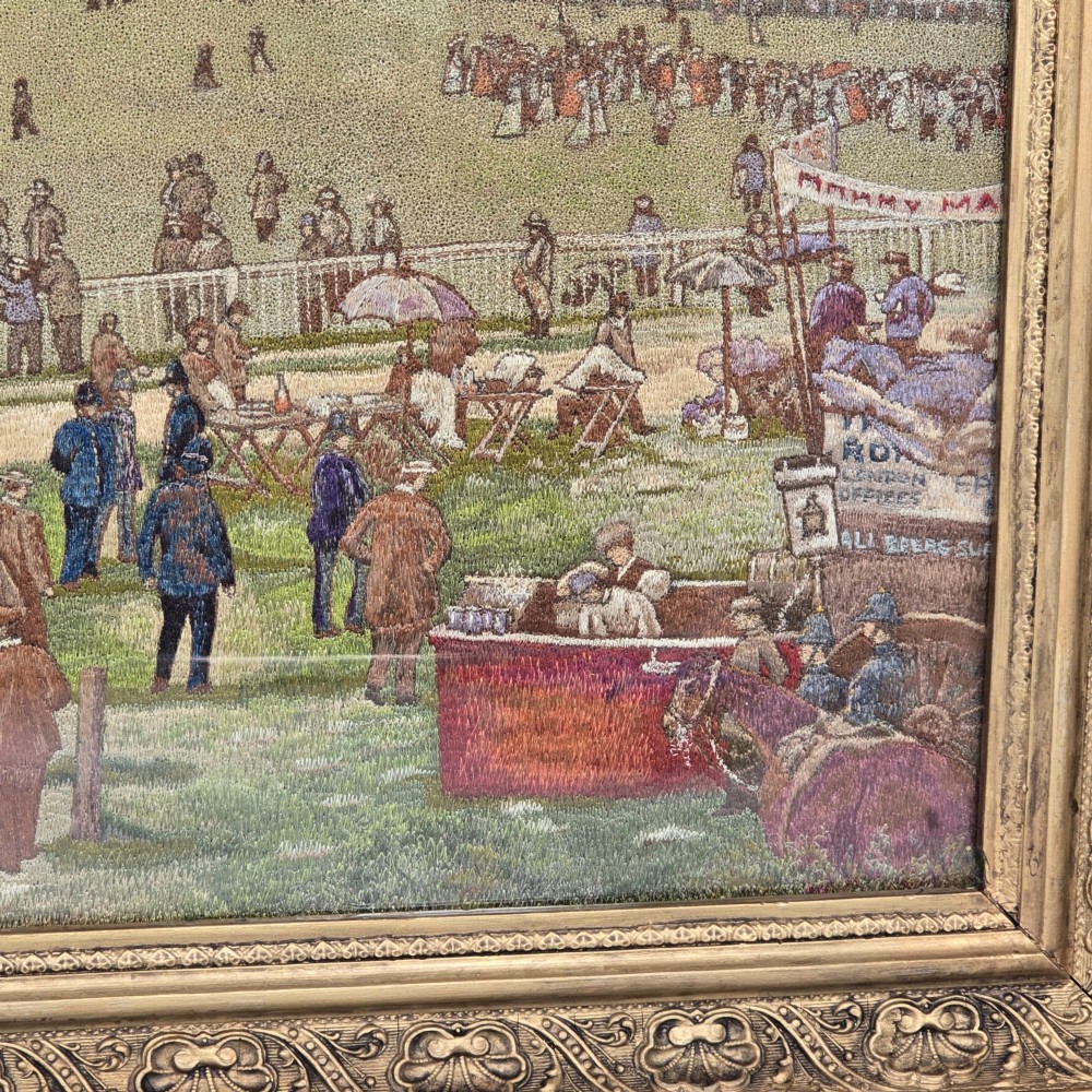 A framed rectangular silk needlework picture depicting figures gathered at the Epsom racecourse within an ornate gilded frame. View III