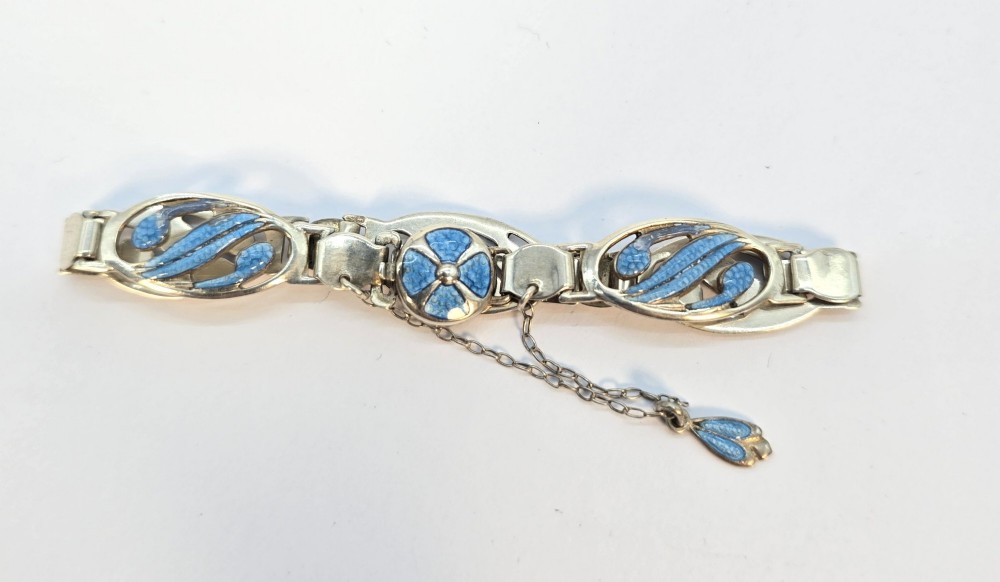 An Edwardian silver link bracelet featuring pierced oval panels filled with light blue enamel and connected by a safety chain.