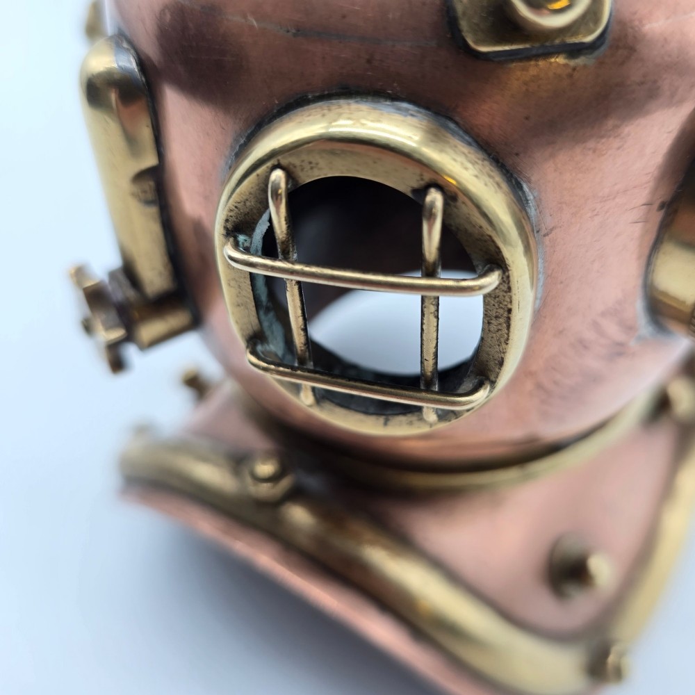 A miniature copper and brass deep-sea divers helmet featuring glass viewports, side valves, and brass shoulder plate studs on a plain white background. View X