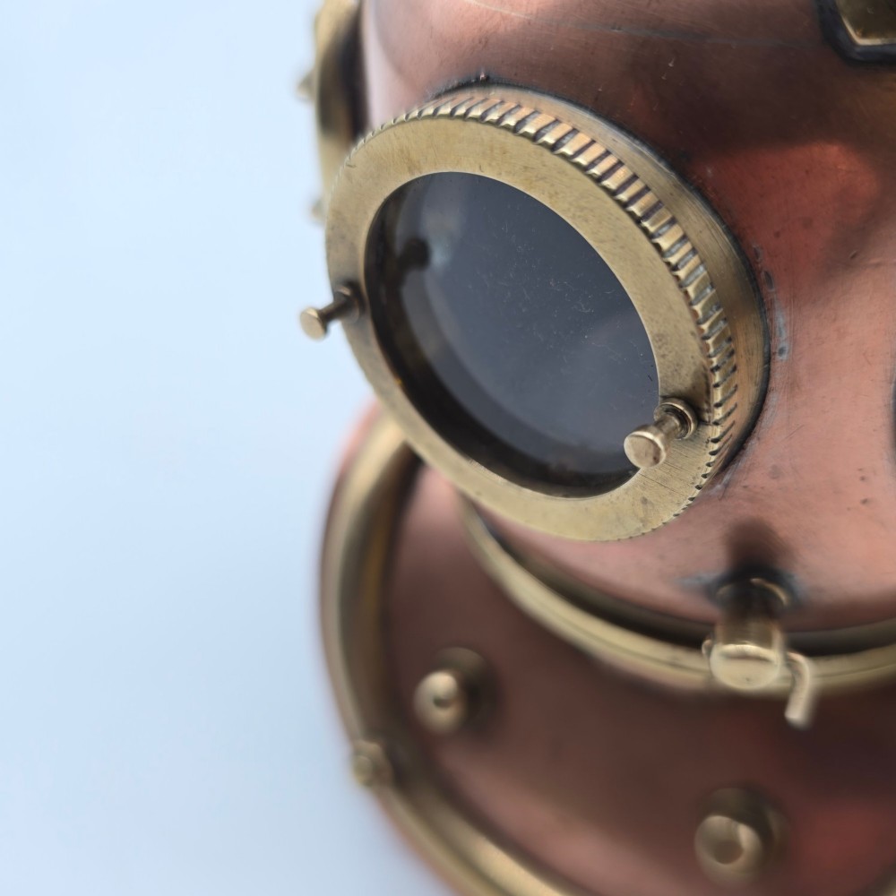 A miniature copper and brass deep-sea divers helmet featuring glass viewports, side valves, and brass shoulder plate studs on a plain white background. View XII