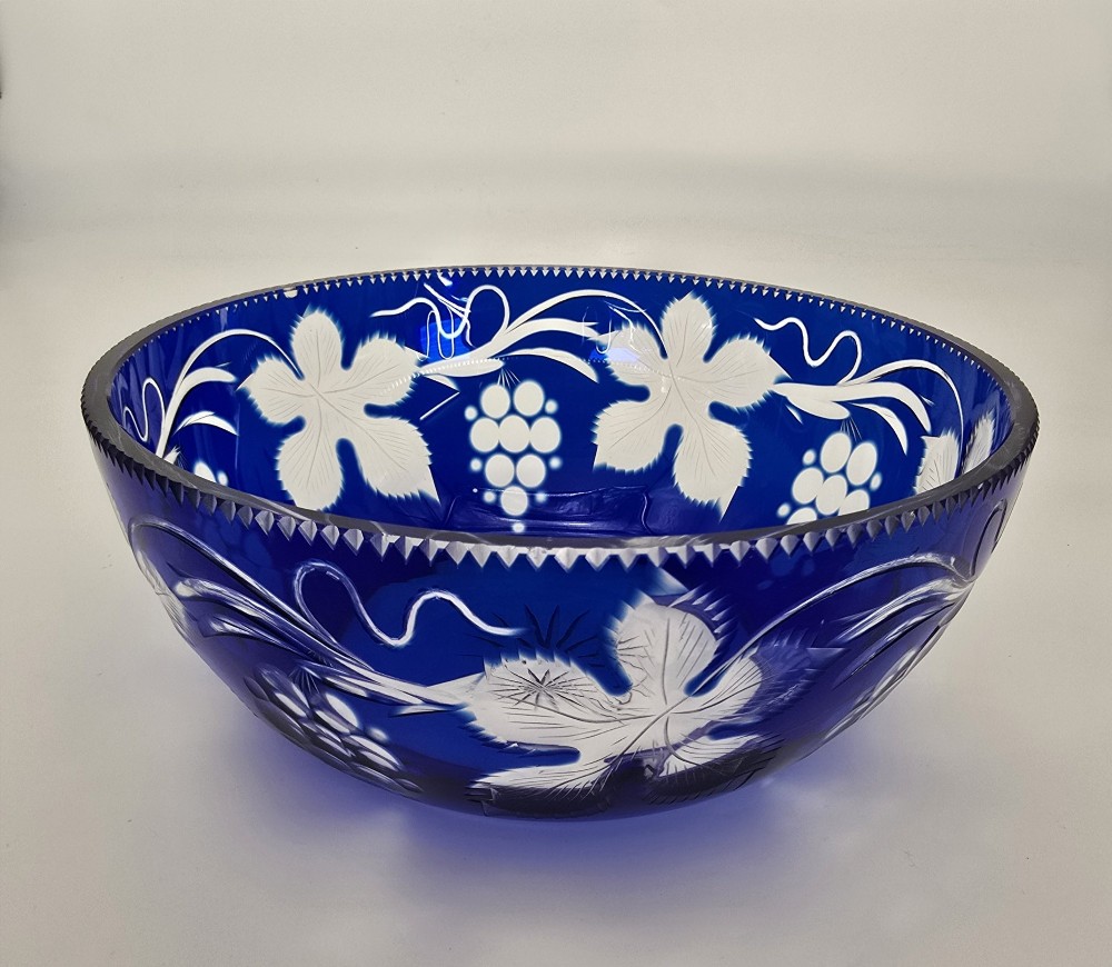 A large round Bohemian cobalt blue cut-to-clear glass bowl featuring etched grapevine leaves, grape clusters, and a serrated rim. View II
