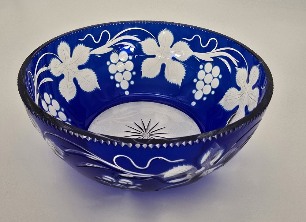 A large round Bohemian cobalt blue cut-to-clear glass bowl featuring etched grapevine leaves, grape clusters, and a serrated rim. View IV