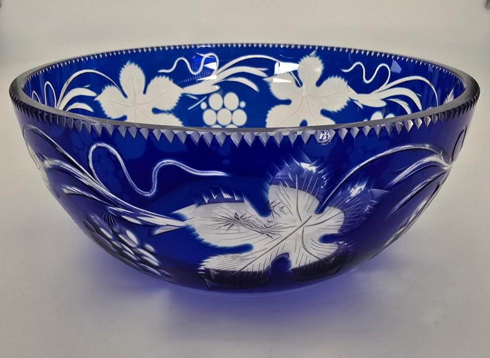 A large round Bohemian cobalt blue cut-to-clear glass bowl featuring etched grapevine leaves, grape clusters, and a serrated rim. View V