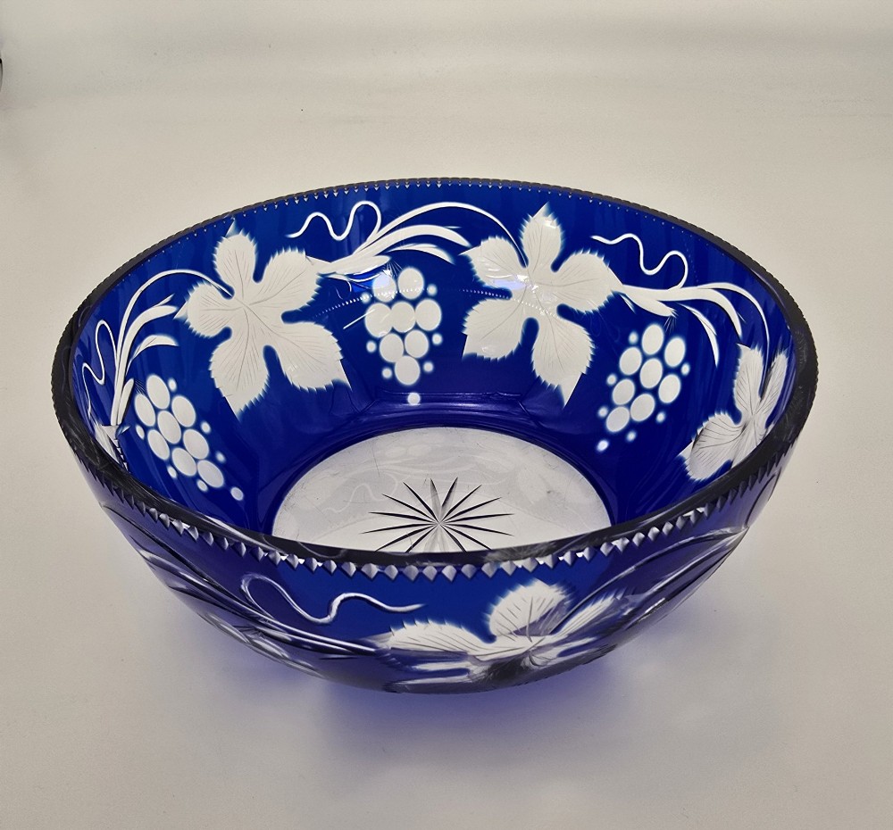 A large round Bohemian cobalt blue cut-to-clear glass bowl featuring etched grapevine leaves, grape clusters, and a serrated rim. View VI